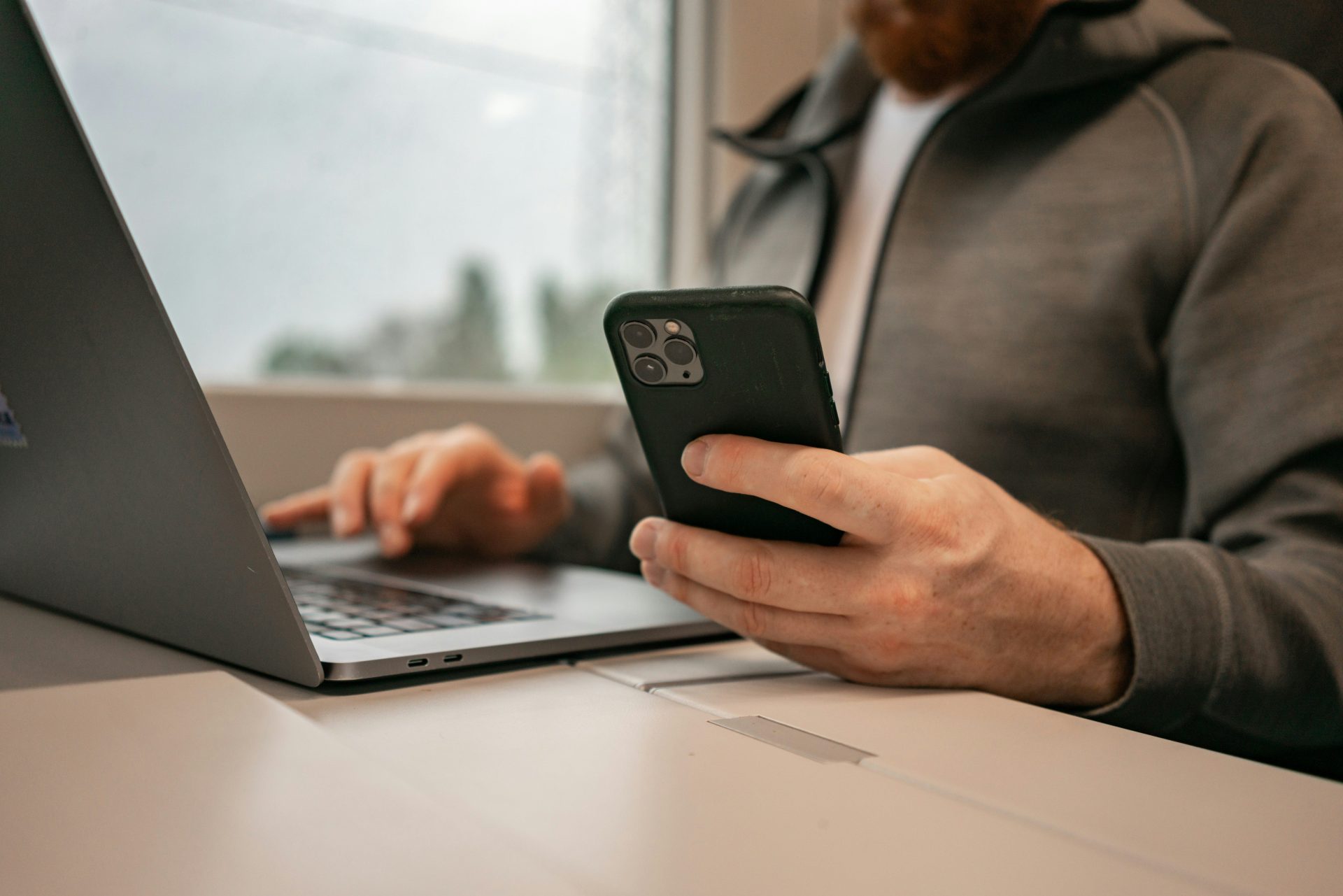 ein Mann, der vor einem Laptop sitzt und ein Mobiltelefon hält